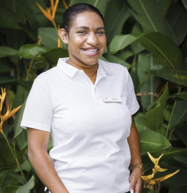Person in a white polo shirt smiling in front of lush green foliage and orange tropical flowers.