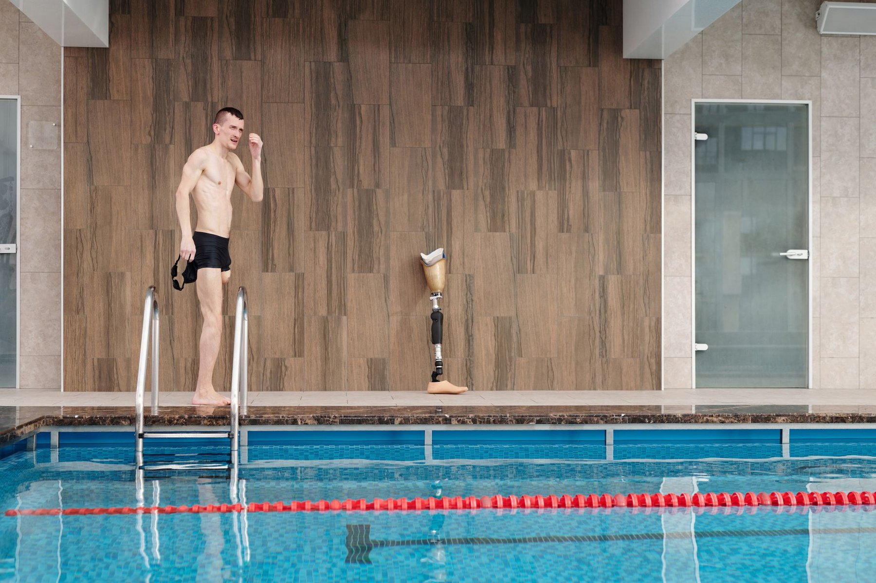 Adaptive athlete with a prosthetic leg standing confidently at the edge of an indoor swimming pool, illustrating accessible swimming for people with disability