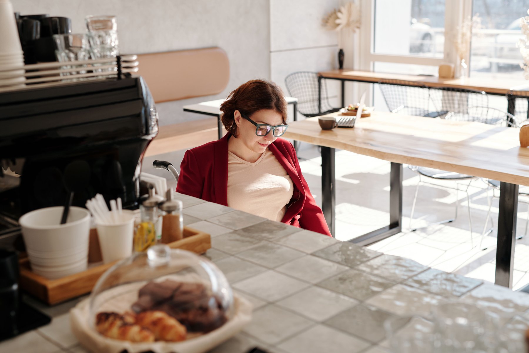 Woman using a wheelchair enjoying coffee and pastries at a bright, modern accessible café counter