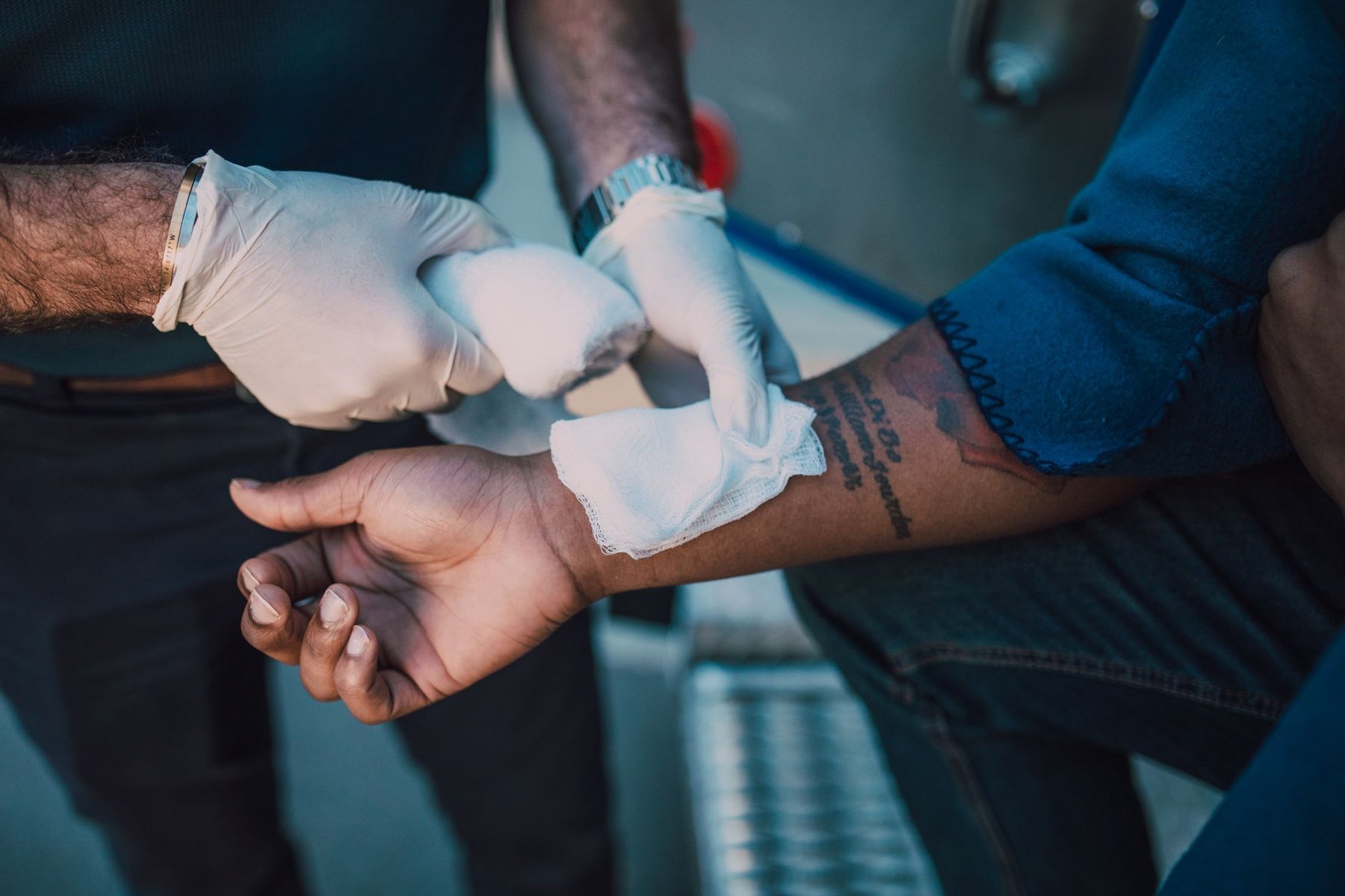 Gloved caregiver carefully applying a sterile bandage to a patient's forearm during complex wound care