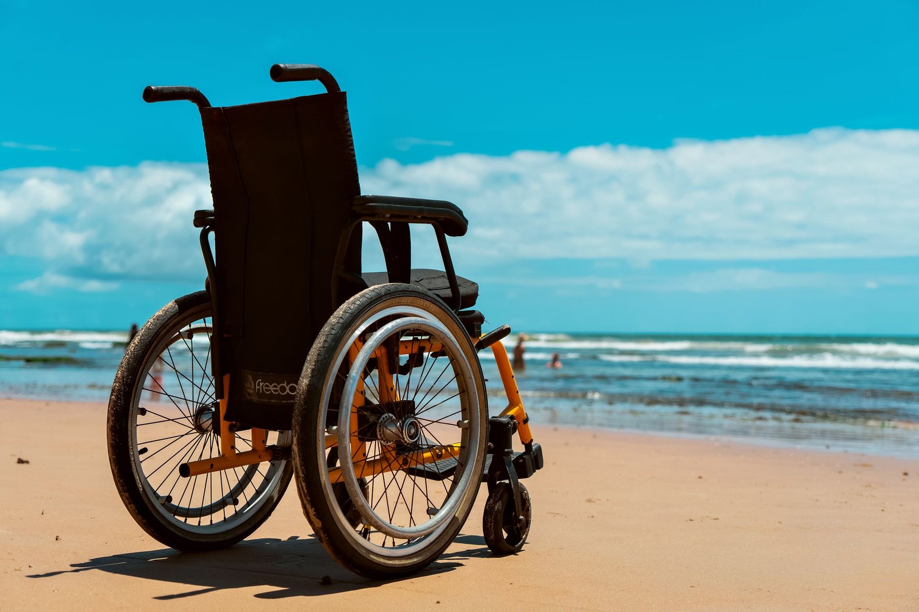 An empty wheelchair on a sunny tropical beach overlooking turquoise ocean waters, symbolizing accessible outdoor spaces for festivals and events