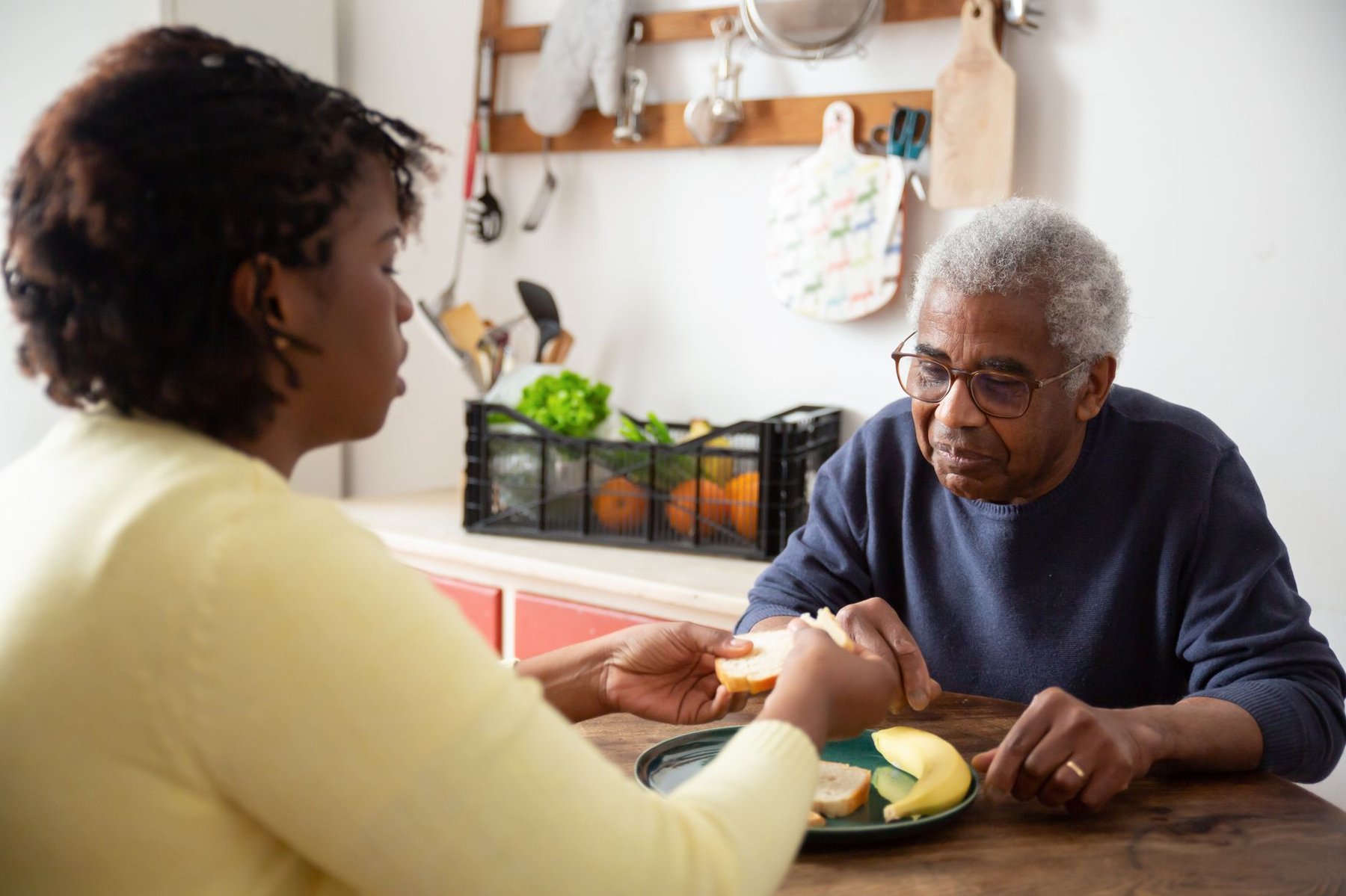 A caregiver gently assists an older man with soft, easy-to-eat foods at home, supporting safe mealtime management.