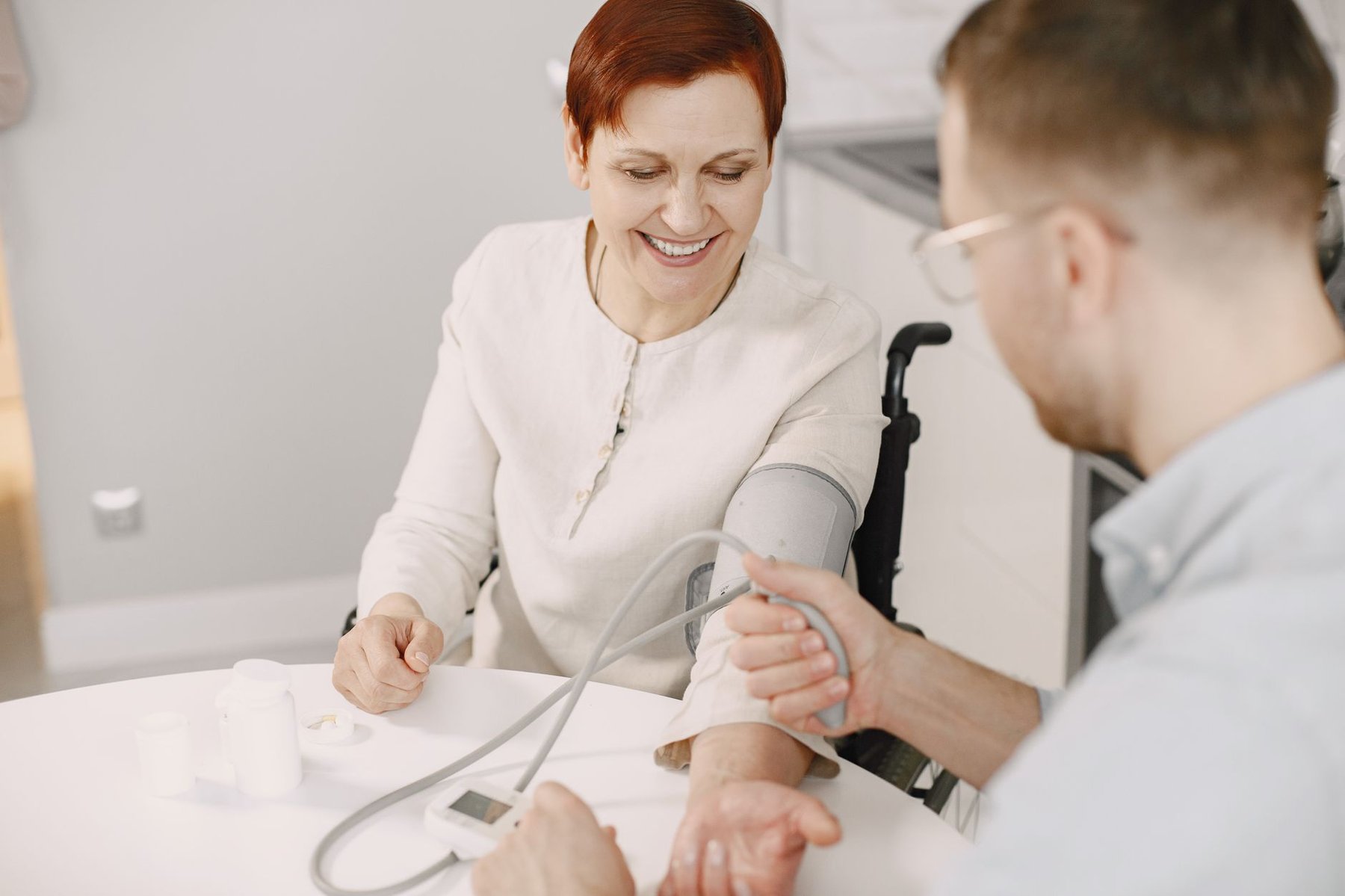 Support worker checking the blood pressure of a smiling woman in a wheelchair at home, showing high intensity NDIS daily living support
