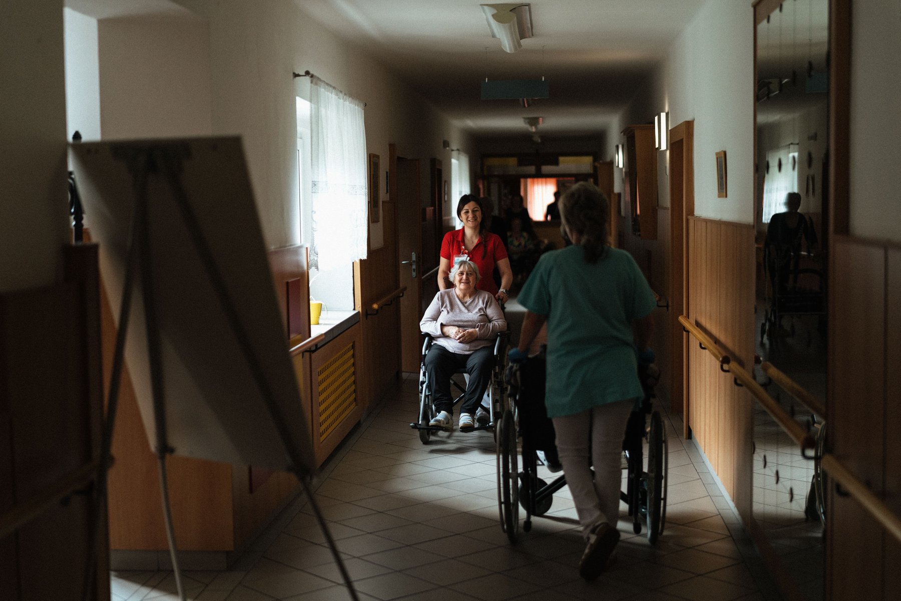 Support worker assisting a person in a wheelchair through a care facility corridor, representing continuous disability support care
