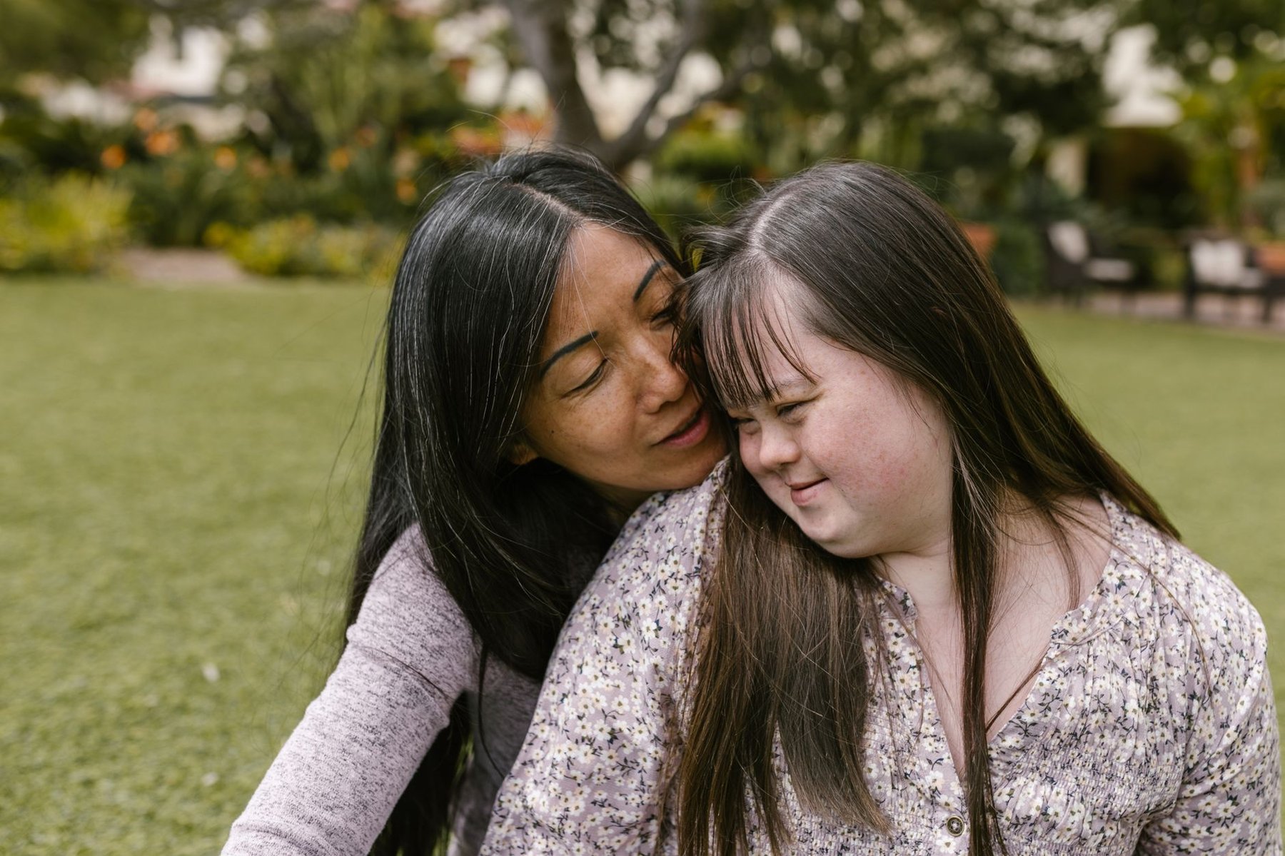 Mother embracing her young adult daughter with Down syndrome in a sunny garden, representing family support through the transition from paediatric to adult disability services