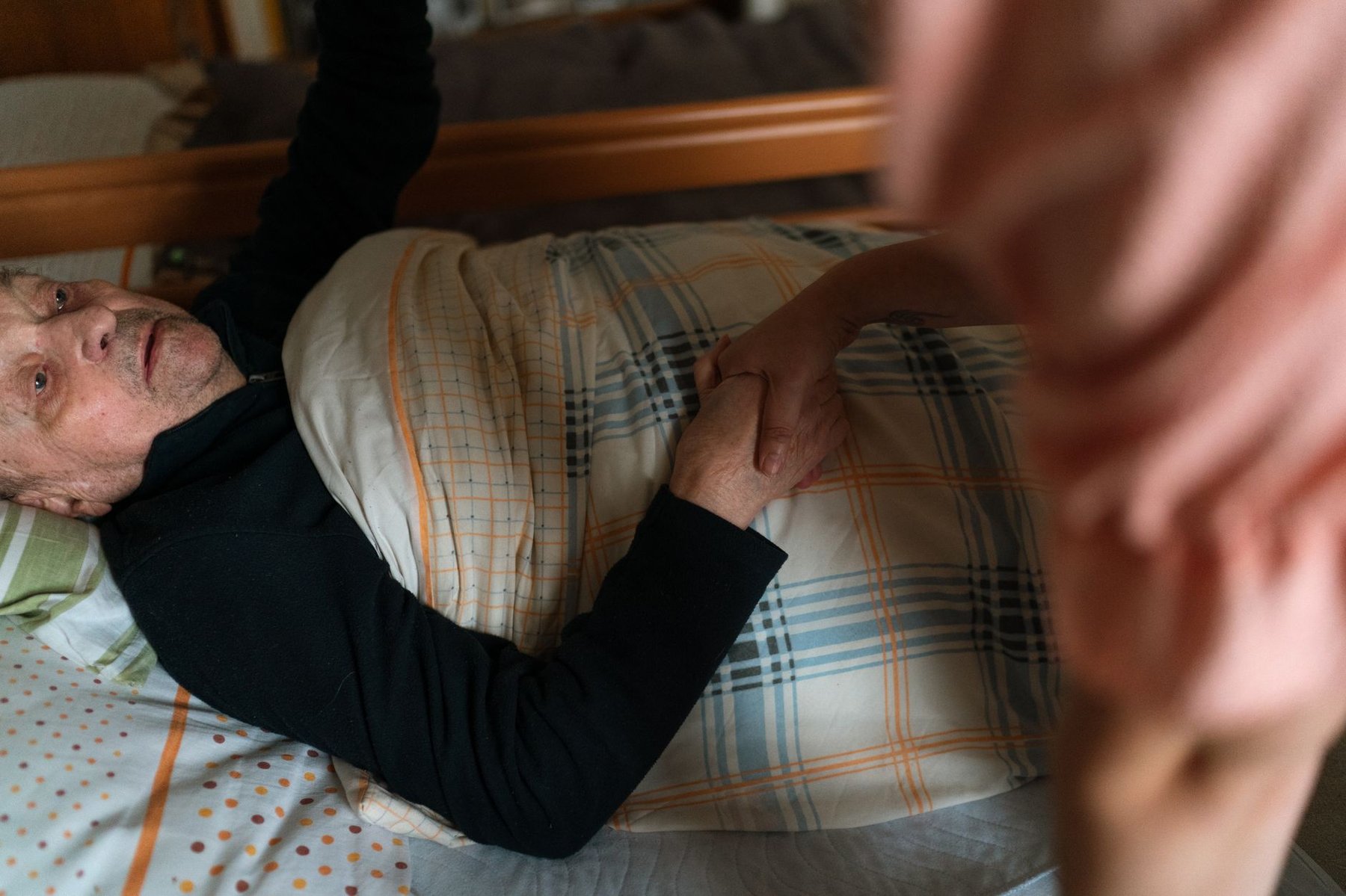 Caregiver gently holding the hand of an elderly man resting in bed at home, offering comfort and support
