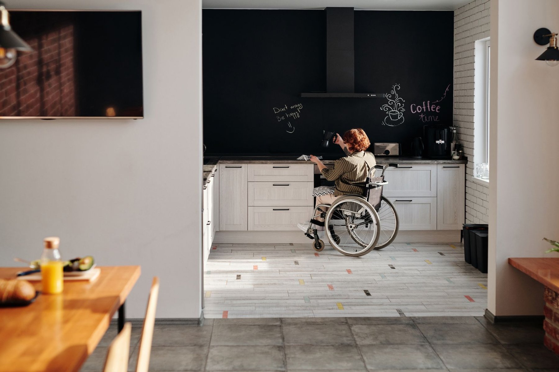 Woman using a wheelchair independently in her sunlit home kitchen after returning home from spinal cord injury rehabilitation