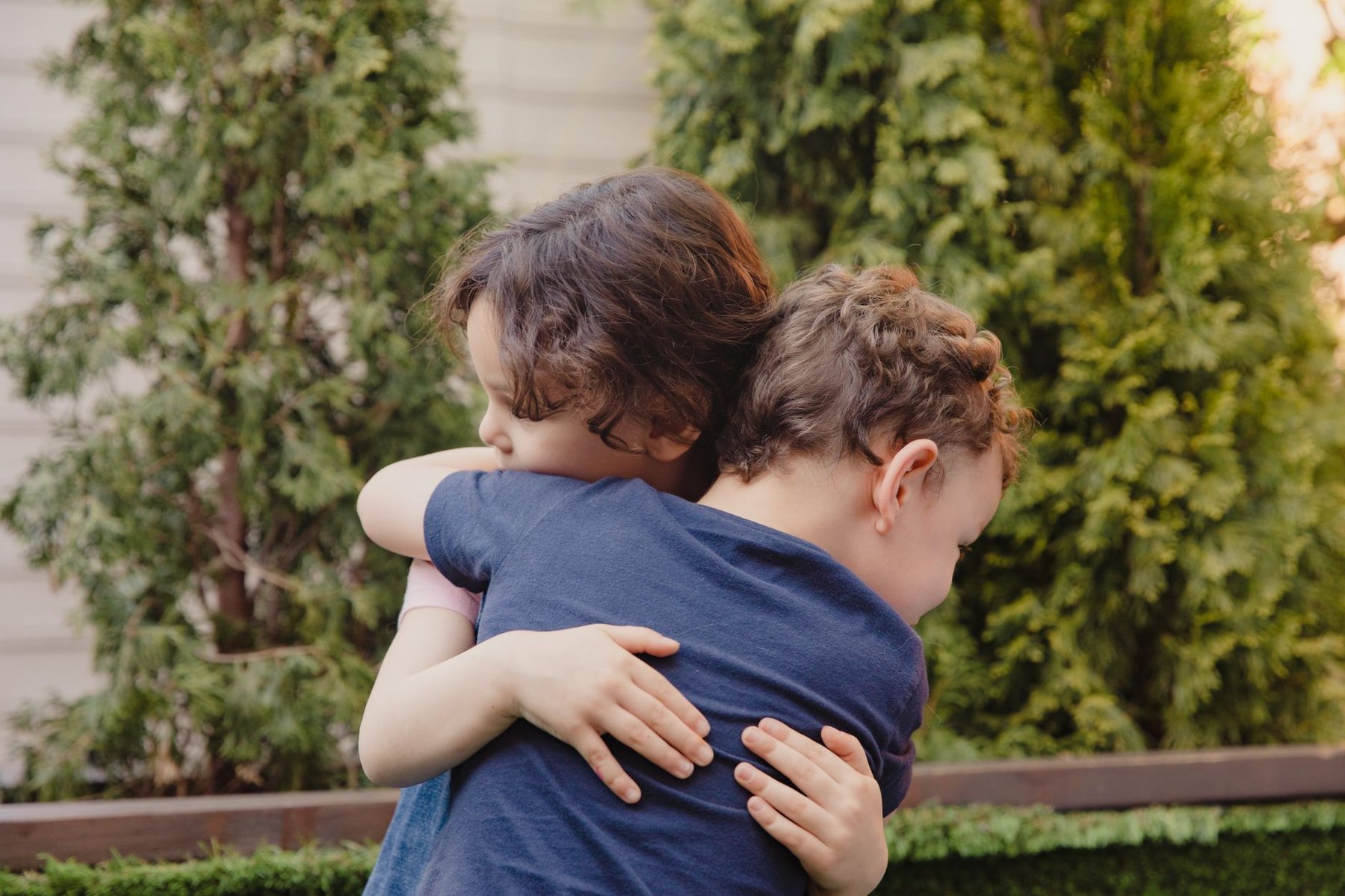 Two young siblings sharing a warm, comforting hug in a garden setting, symbolizing emotional support between brothers and sisters
