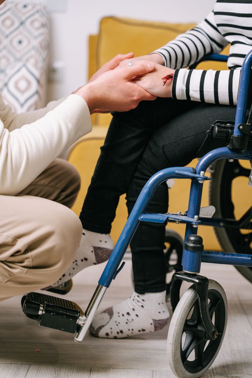 Support worker gently holding the hand of a client in a wheelchair, offering compassionate care
