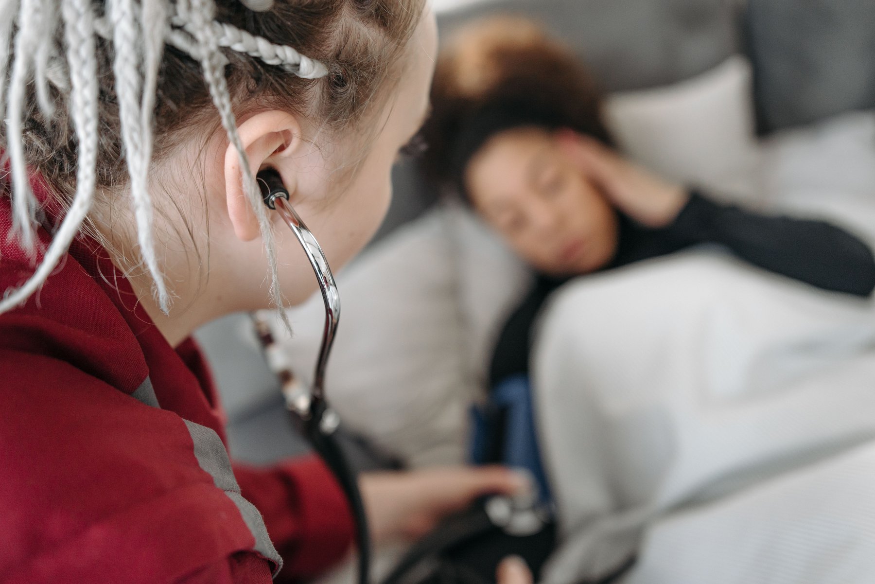 Home health nurse using a stethoscope to check on a patient resting in bed at home