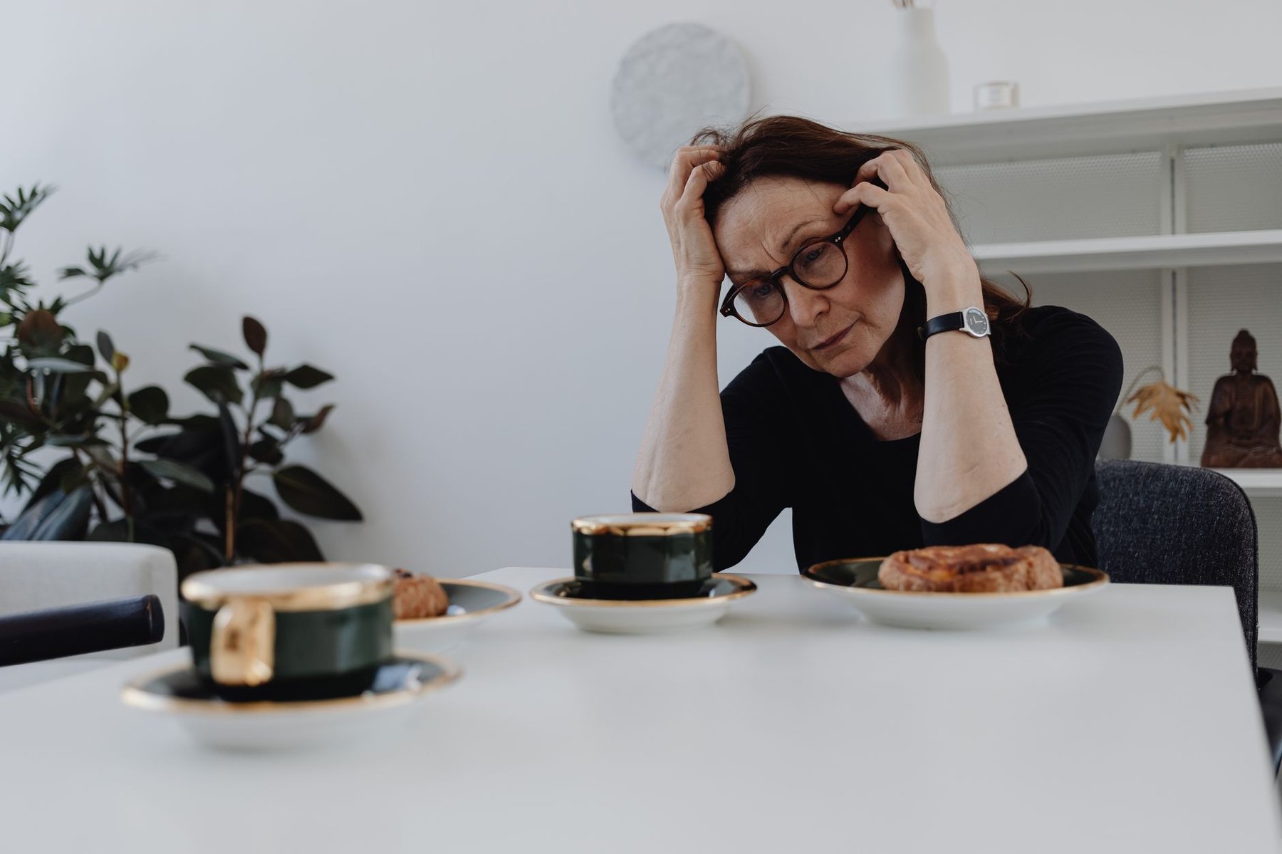 Middle-aged woman at a kitchen table holding her head in confusion, reflecting the early signs of young onset dementia and the need for NDIS support